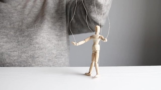 Puppet. Women's hands control a wooden man model toy using threads on a grey background. Manipulating arm on a gray background