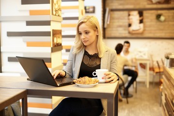 Fototapeta na wymiar Blonde woman using laptop in internet cafe
