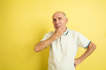 Thoughtful. Caucasian senior man's portrait isolated on yellow studio background. Beautiful male emotional model. Concept of human emotions, facial expression, sales, wellbeing, ad. Copyspace.