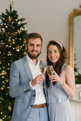 Attractive and loving man and girl on the background of the Christmas tree at home with glasses of champagne, the concept of Christmas love story