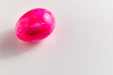 Bright pink easter egg with some first fine little cracks in the eggshell lying on white ground with copy space