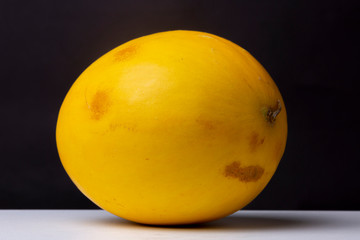 Smooth yellow Canary melon on a white surface against an out of focus dark grey background