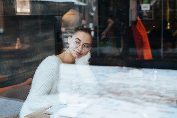 shot through the glass of a cafe where a pensive student in glasses for vision sits