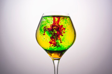 Red , green and yellow food coloring diffuse in water inside glass , with gradient background
