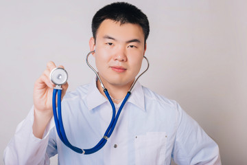 Asian doctor in a white coat with a stethoscope on a white background. Studio portrait of a handsome guy in white medical clothes