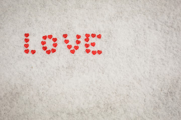 The word Love is made of red glass hearts on white snow. Symbols for Valentine's day, background with snow texture and hearts