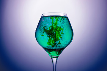 blue and green food coloring diffuse in water inside glass , with blue background