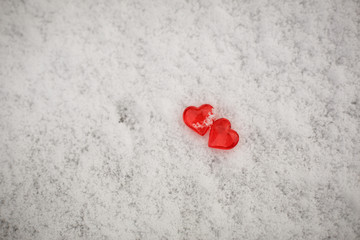 Fototapeta premium Two red glass hearts on the snow. Symbols for Valentine's day, background with snow texture and hearts