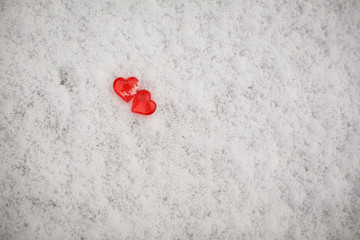 Two red glass hearts on the snow. Symbols for Valentine's day, background with snow texture and hearts