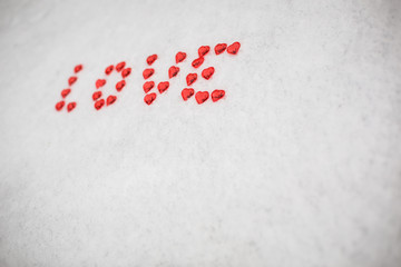 The word Love is made of red glass hearts on white snow. Symbols for Valentine's day, background with snow texture and hearts