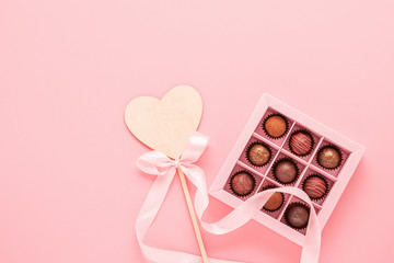 Chocolates truffle in a craft box pink background and a wooden heart on a pink background.