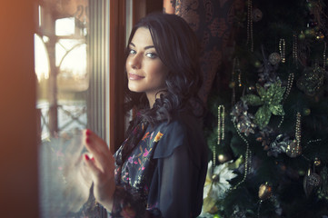 Beautiful woman in evening dress near Christmas tree