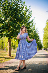 Girl with red lips and a dress in peas on a background of trees in the park. Pin-up model.