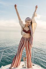 girl stands on a boat against the background of the ocean, arms raised triumphantly
