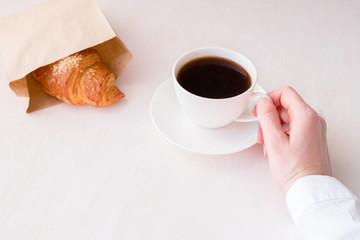 White cup with coffee in hand on a white background and fresh croissant
