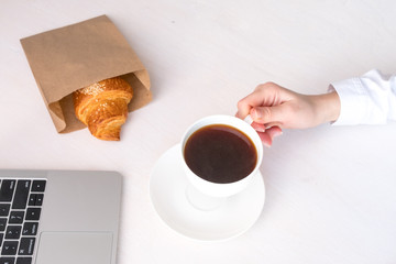 White cup with coffee in hand on a white background and fresh croissant