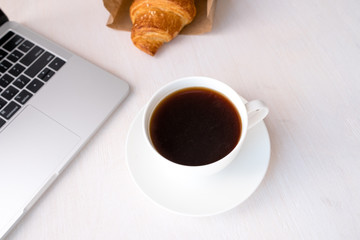 Cup of coffee from a laptop computer with fresh croissants. on white background.concept of education