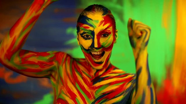 Color face art and body paint on woman dancing in slowmotion. Abstract portrait of the bright beautiful girl with colorful make-up and bodyart.