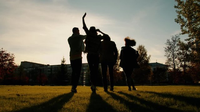 Back view of joyful students girls and guys walking dancing doing high-five outdoors in city in autumn evening. Happiness, friendship and lifestyle concept.