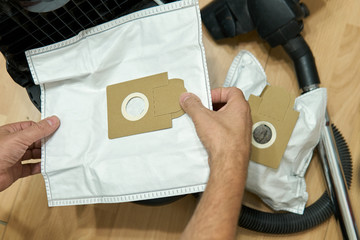 New dust bag in male hands above of a vacuum cleaner during the dust bags replacement