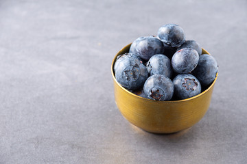 Close-up of blueberries in golden bowl on dark background in horizontal with copy space