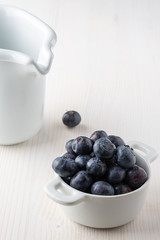 Top view of blueberries in white bowl, one more on white background, with white milkmaid in the background and copy space