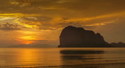 view seaside evening of mountain on the beach with orange and red sun light in cloudy sky background, sunset at Pak Meng Beach, Trang Province, southern of Thailand.