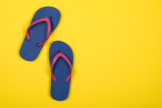 Pink and blue flip flops on a yellow background with copy space