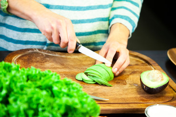 Woman cuts a green avocado into slices