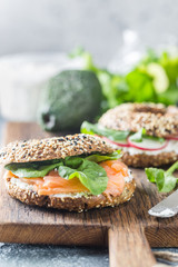 Bagels with cream cheese avocado, fish, arugula and radish on old wooden table. Healthy breakfast food.