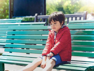 Outdoor portrait of  Sad Kid sitting alone metal fence, Emotional portrait of Upset boy looking down with thinking face, Lonely child with bored face, Spoiled children concept