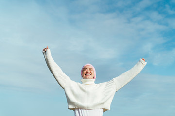 Portrait of happy young woman with cancer with arms up