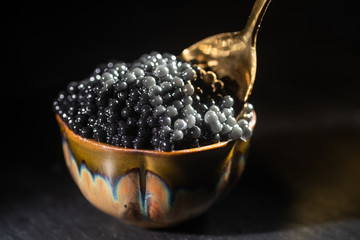 Jar of black caviar and spoon with black caviar on dark background