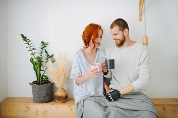 Happy husband and wife sitting together on a shelf, drinking coffee at home.