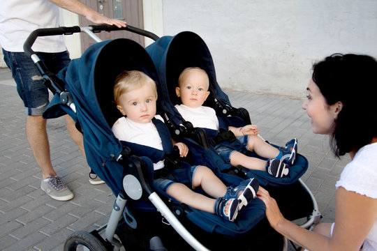 Young mother stop the buggy and  slook to the twins on buggy. People walking on the street .