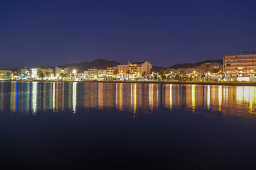 Panoramic view on seaside town and calm sea on a dramatic night sky background. Beautiful, amazing, great night over the bay of Roses, Catalunya, Spain. Reflections on the water.