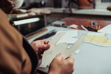 cropped view of cobbler holding paper template in workshop