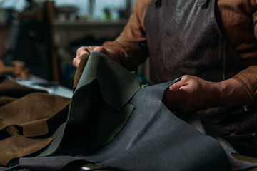 partial view of shoemaker holding piece of genuine leather in workshop - obrazy, fototapety, plakaty