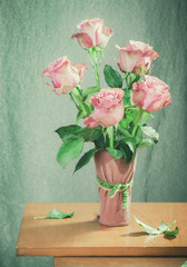 bouquet of pink roses on a light green background in a pink vase on a wooden table
