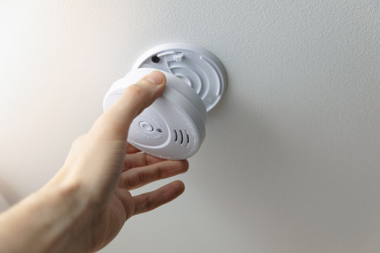 hand installing smoke detector on the room ceiling