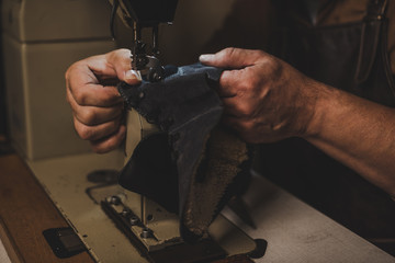 cropped view of cobbler sewing part of leather shoe on sewing machine