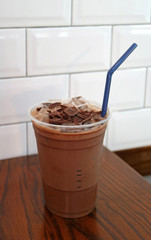 Iced chocolate topped with chocolate chunks in takeaway cup isolated on wooden table