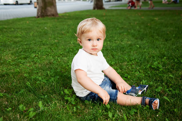 Alone baby sit on the green gras on the park. the kid wearing jeans and white t-shirt