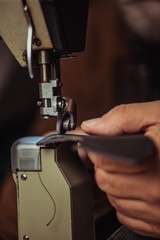 cropped view of cobbler sewing genuine leather on sewing machine