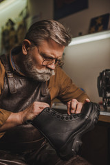 attentive, senior shoemaker holding leather boot in workshop