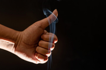 A close up of a man's hand showing a thumbs up and smoky black background