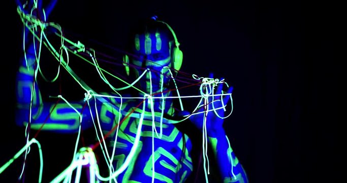 Big man with headphones and body art is holding glowing strings, 4k