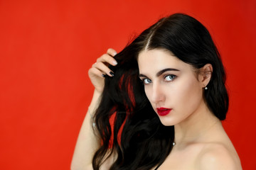 Fototapeta premium The concept of long beautiful hair. Close-up Portrait of a pretty brunette model girl with excellent makeup and luxurious hair on a red background in the studio.