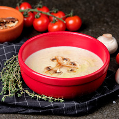 Bowl of mushroom cream soup with fried champignon mushrooms and vegetables on black stone background. Rustic style. Close up.