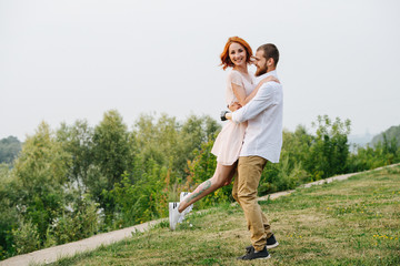Happy married middle age couple having fun in a park next to a river. Man is spinning with wife in...